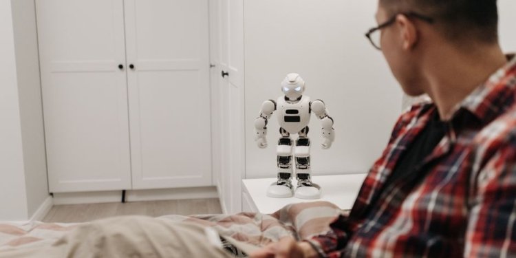 A man examines a robotic toy placed on a table in a contemporary bedroom setting.